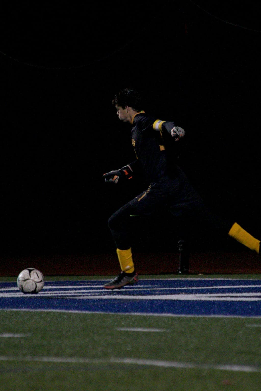Photo of a goalkeeper kicking a ball on a floodlit pitch at night